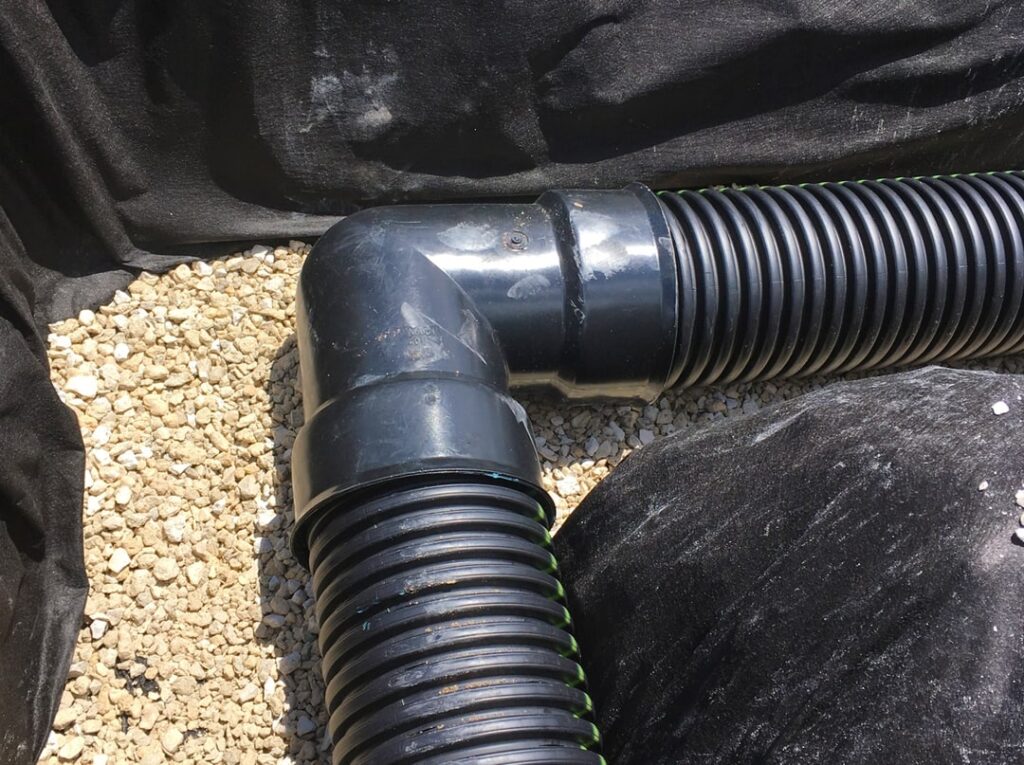 image of black elbow joint in drainage pipe in ground, exposed