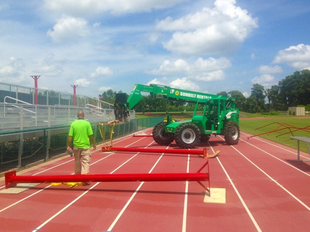 image of a man working with a crane to erect poles around running track