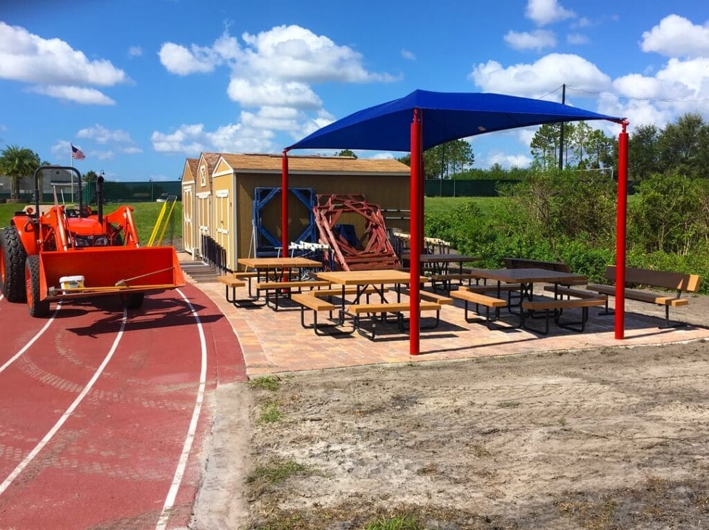 site work being done to install blue shading structure above picnic tables next to running track