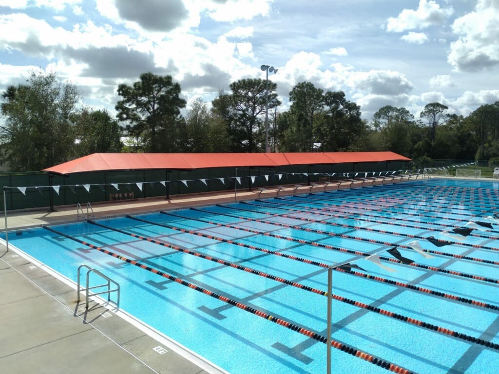 image of large blue, pool with lanes and red shading structure along pool deck