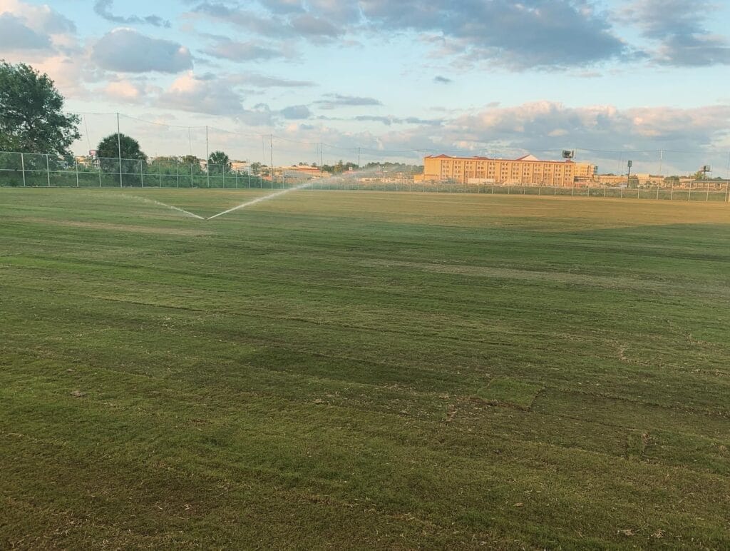 image of sprinklers spraying on recently completed natural grass soccer field, building in background