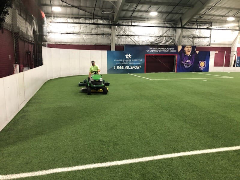 man driving tractor using device to groom the synthetic turf field, he looks ahead