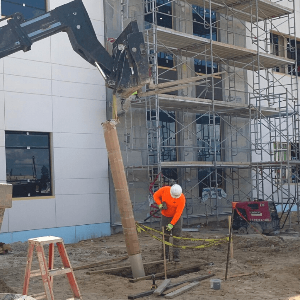 man in hardhat installing large column into footer in ground