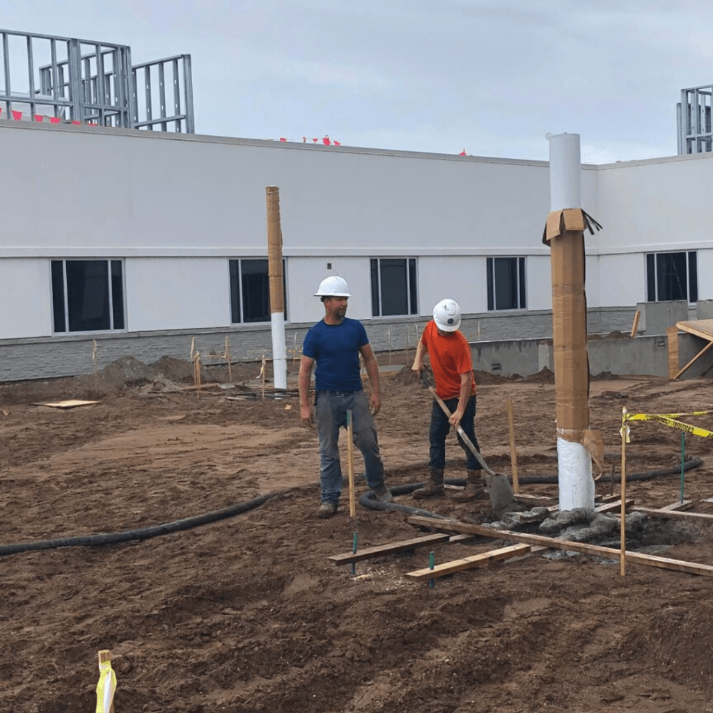 two men stand next to large column placed in a footer in the ground.